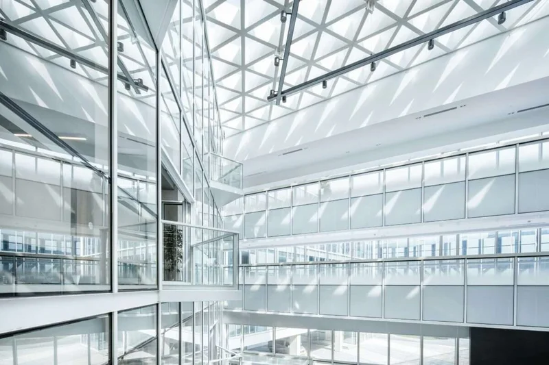 Atrio corporativo iluminado com claraboia geometrica e passarelas em multiplos pavimentos — escritorio hybrid
