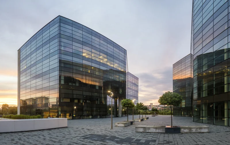 Conjunto corporativo de torres em vidro espelhado ao entardecer com calcamento em pedra — arquitetura empresarial premium