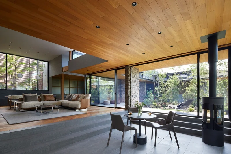 Interior de uma casa japonesa contemporânea com grandes painéis de vidro que se abrem para um jardim interno.