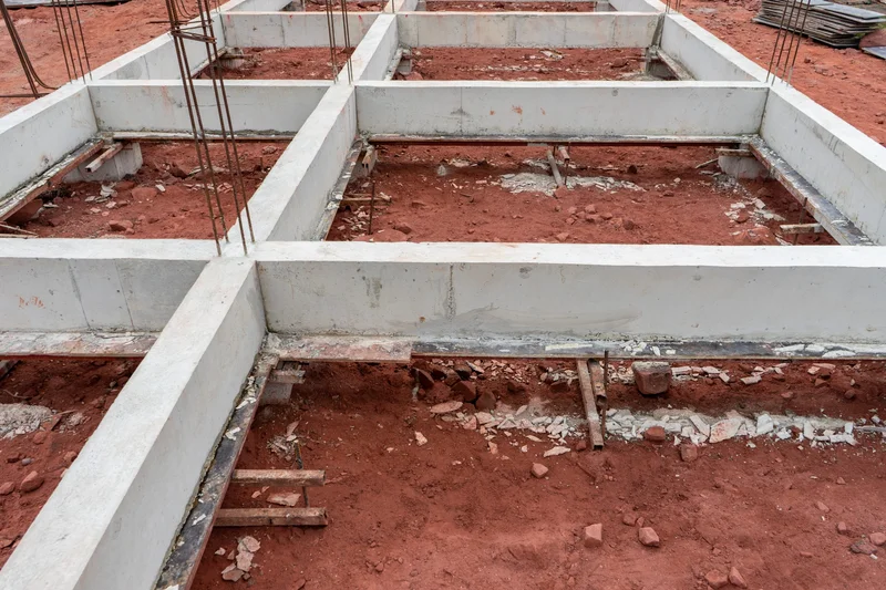 Vigas baldrame concretadas em obra residencial brasileira ligando sapatas isoladas sobre solo de argila vermelha