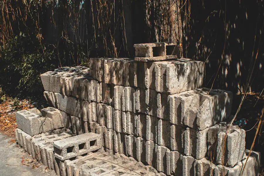 Pilha de blocos de concreto vazado descansando em canteiro de obra — peça pesada de 13 kg com furos verticais para graute e ferragem