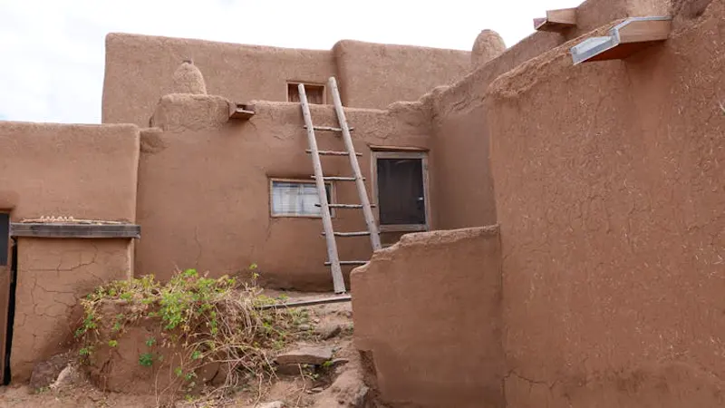 Construção em adobe no Pueblo de Taos, Novo México — paredes de terra crua e escada de madeira tradicional