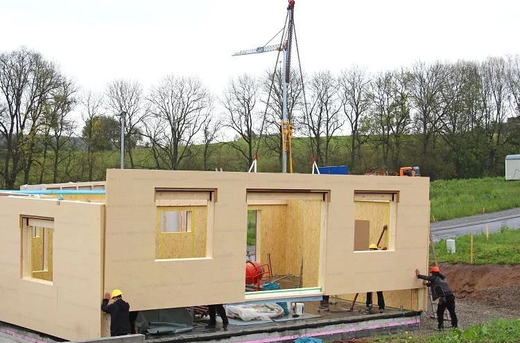 Montagem real de casa pré-fabricada em wood-frame com guindaste içando painéis estruturais para encaixe sobre fundação concretada