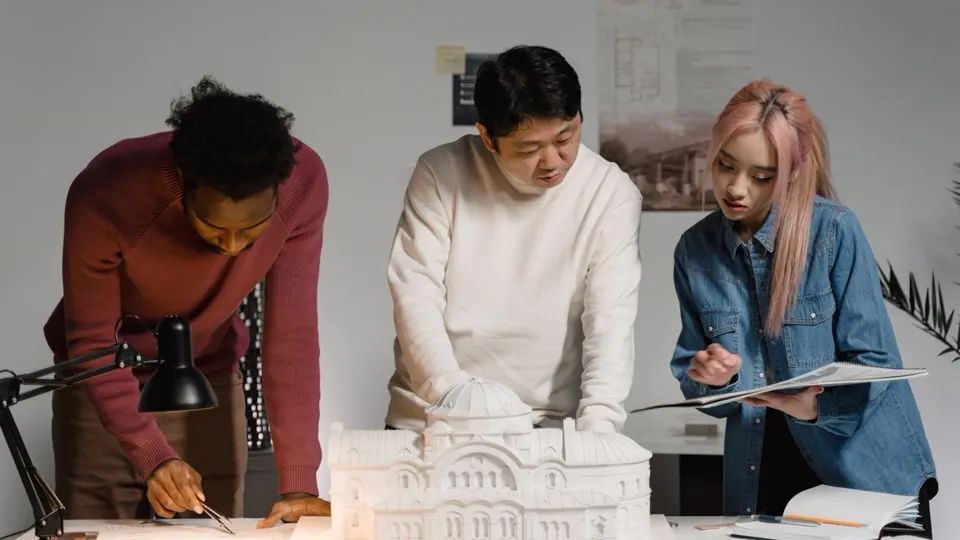 Trio de arquitetos trabalhando em maquete de edificação — networking e trabalho em equipe