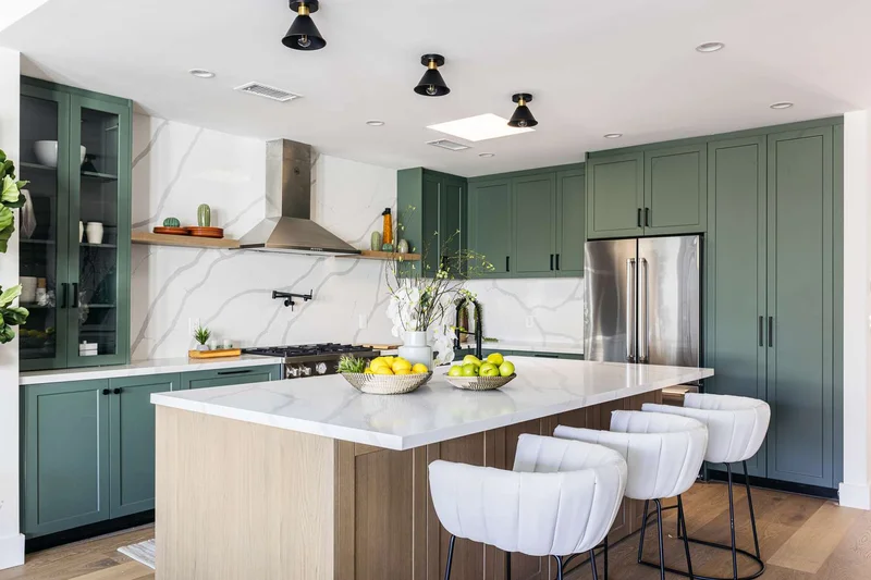 Cozinha americana com bancada e parede em quartzo prensado branco veiado, armários verde escuro e cooktop com coifa de aço
