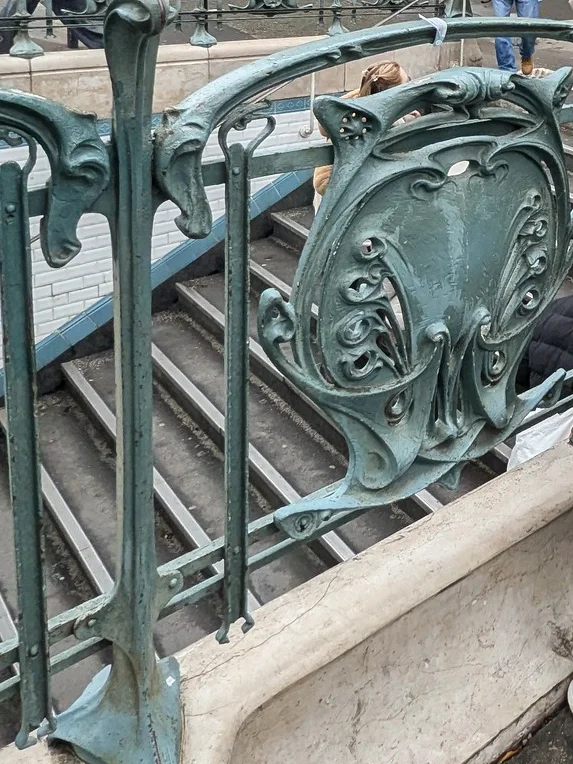 Detalhe de uma grade de ferro forjado no estilo Art Nouveau com motivos de folhas e flores.