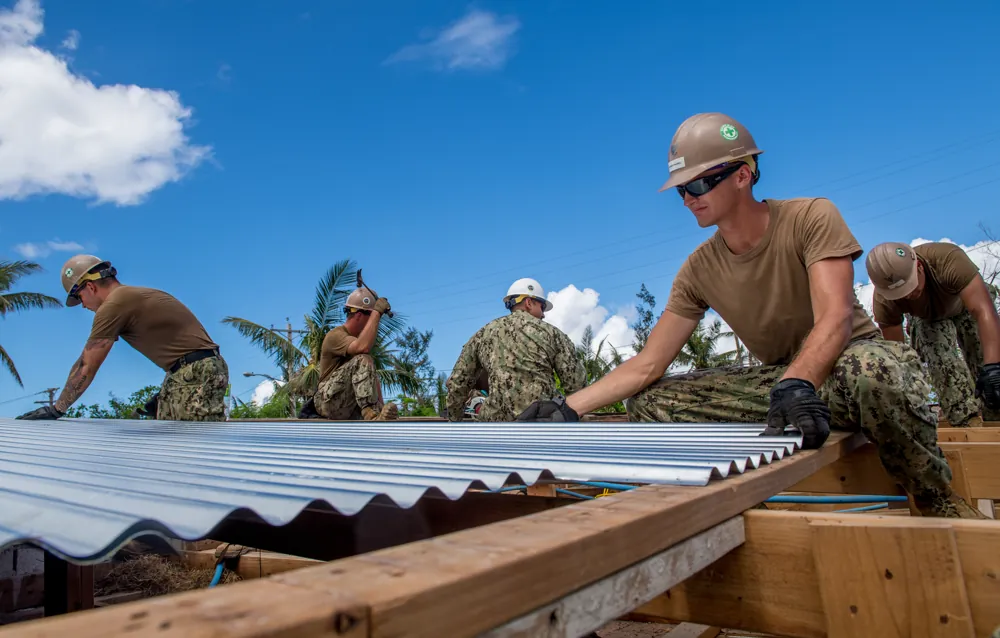 Equipe instalando chapas metálicas trapezoidais sobre estrutura de telhado em obra de galpão