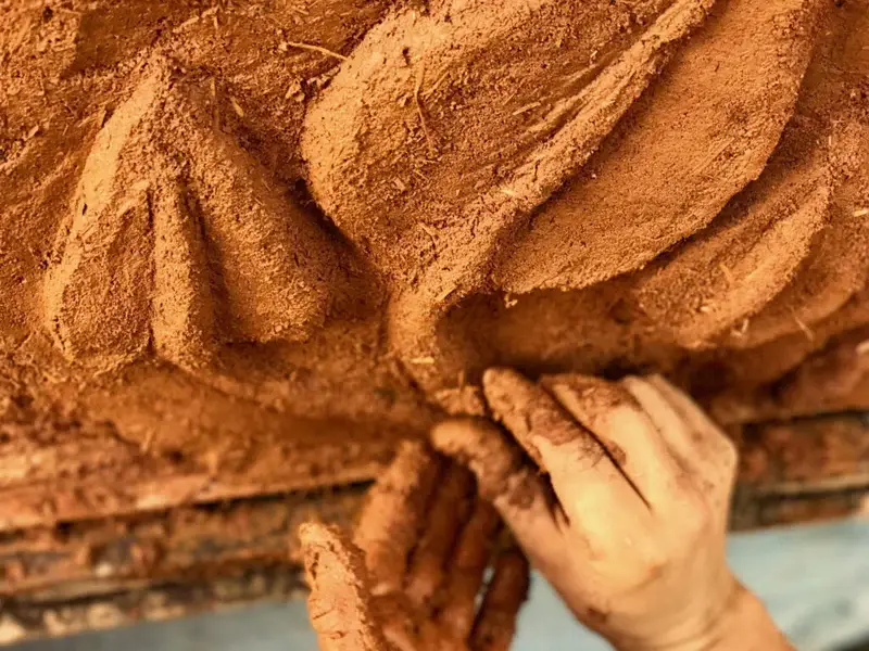 Artesão modelando parede de adobe à mão em obra com material sustentável de terra crua, exemplo de taipa contemporânea
