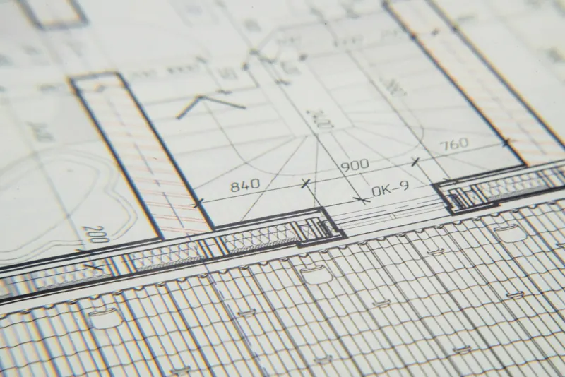 Especificações técnicas em papel sobre mesa de arquitetura, com planta ao fundo
