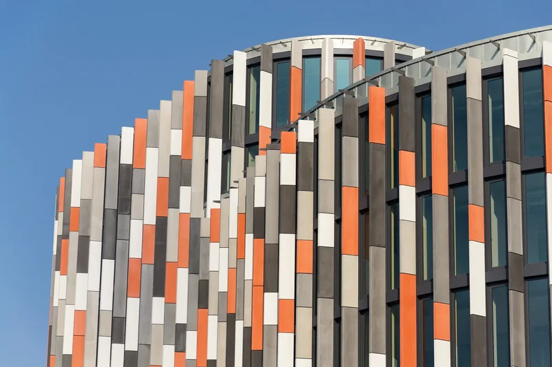 Fachada de edifício comercial com brise vertical misto em painéis coloridos contra céu azul — exemplo de proteção solar diversificada por orientação