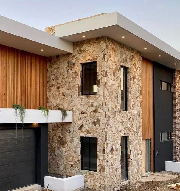 Fachada de uma casa moderna com revestimento externo de pedra natural e detalhes em madeira.